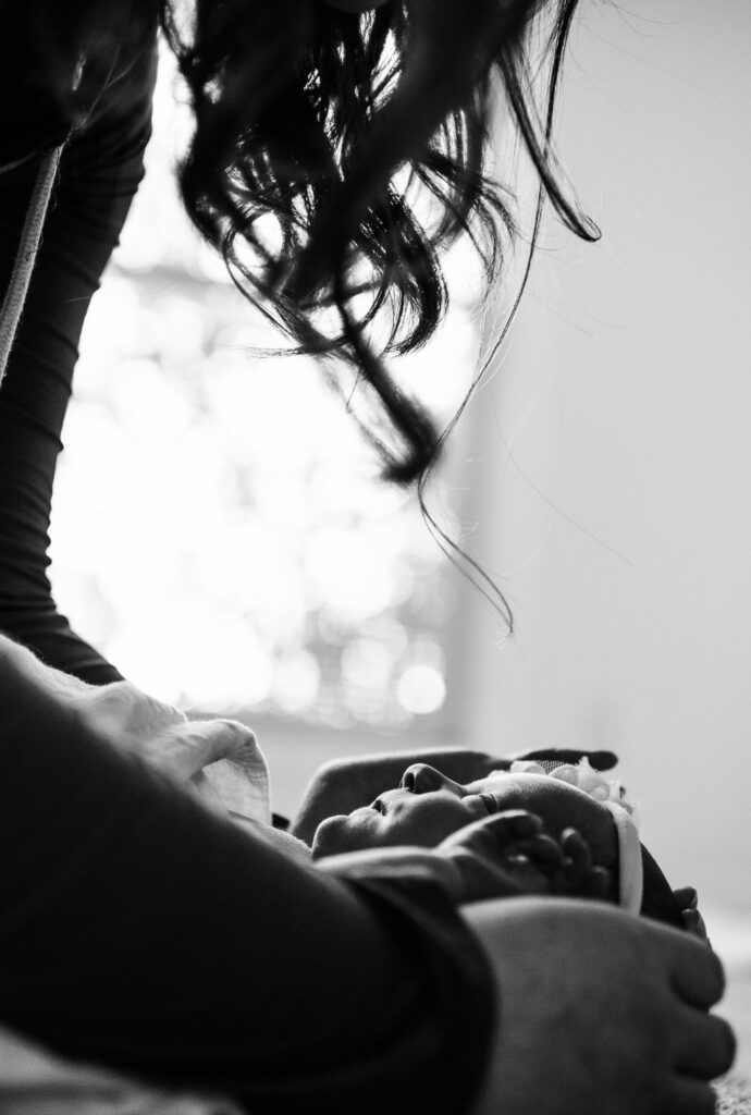 mother looking down at newborn wearing bow silhouette in window