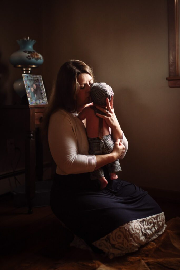 mother embracing newborn wearing hat and suspenders in Columbia, MO