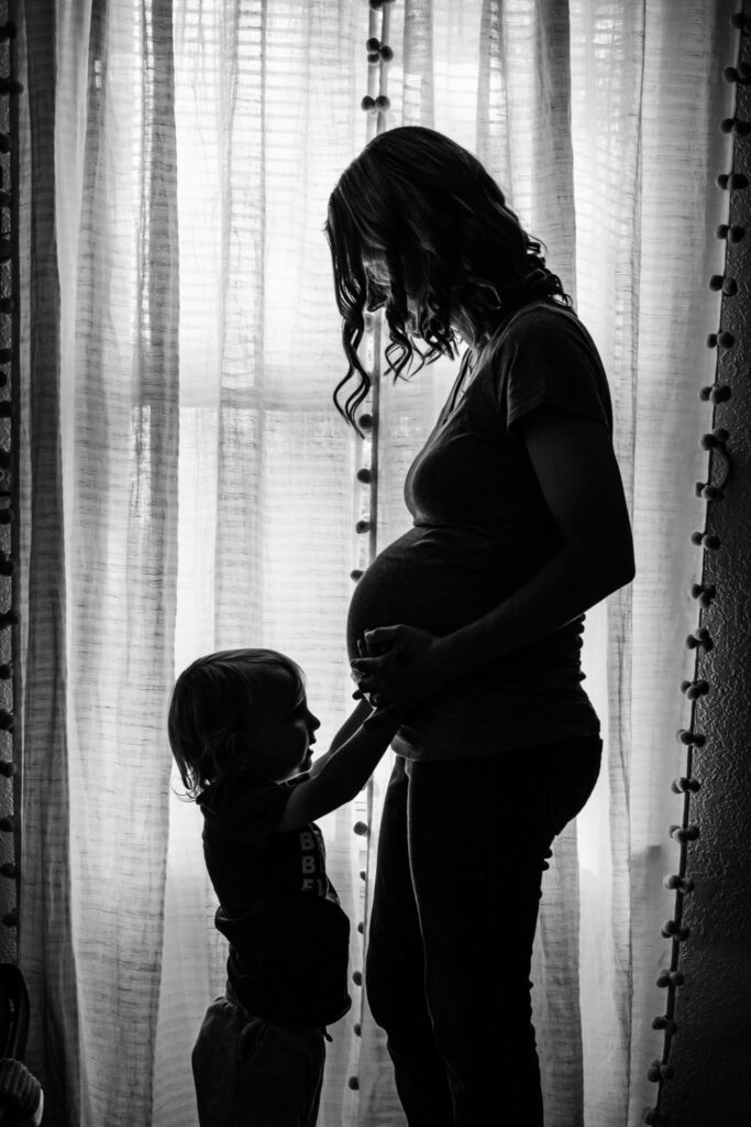 son holding mother's pregnant belly in front of curtains