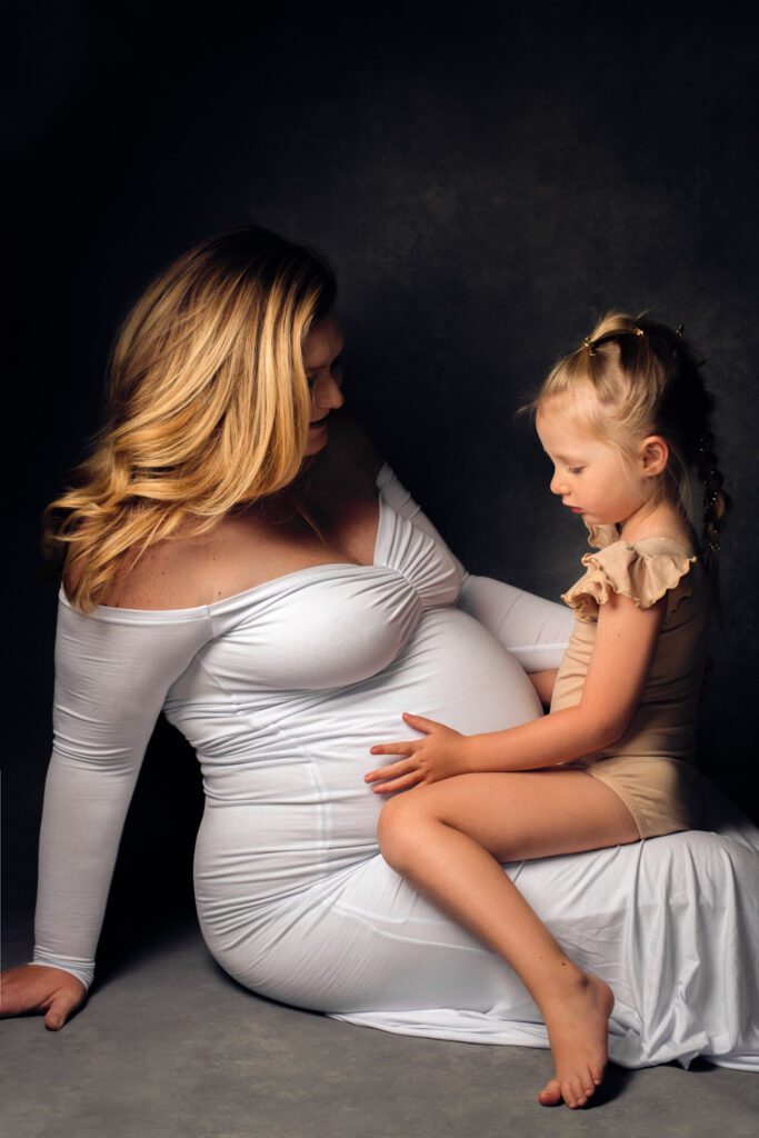 pregnant mother with daughter on lap holding belly
