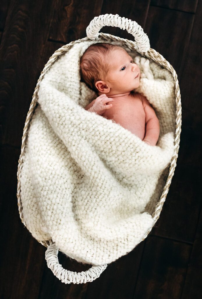 naked newborn wrapped in blanket in basket on floor