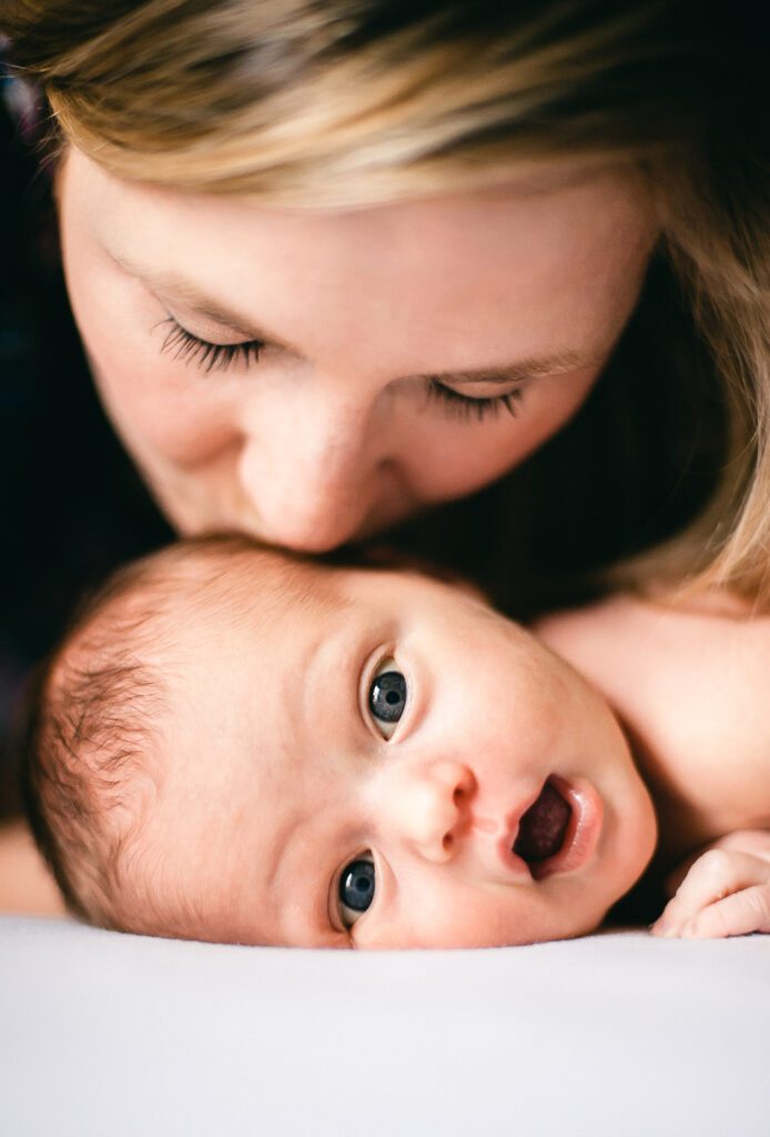 newborn looking surprised while getting kiss from mom