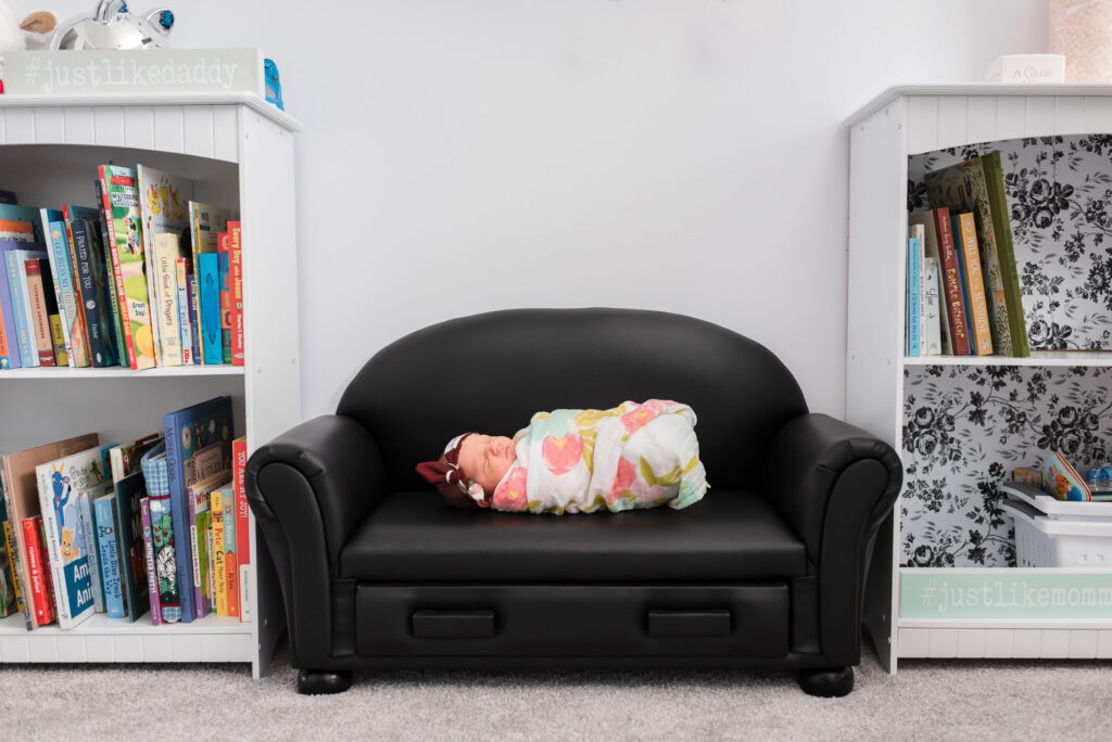newborn swaddled on tiny couch between books shelves in Columbia, MO