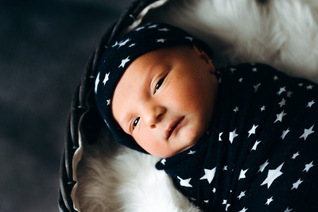 newborn wrapped in star swaddle laying on fur blanket in basket