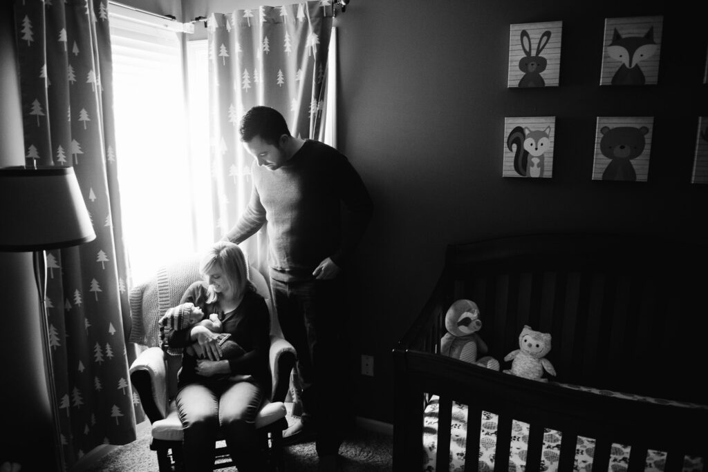 mother holding newborn in rocking chair by window in the shadows in Columbia, MO