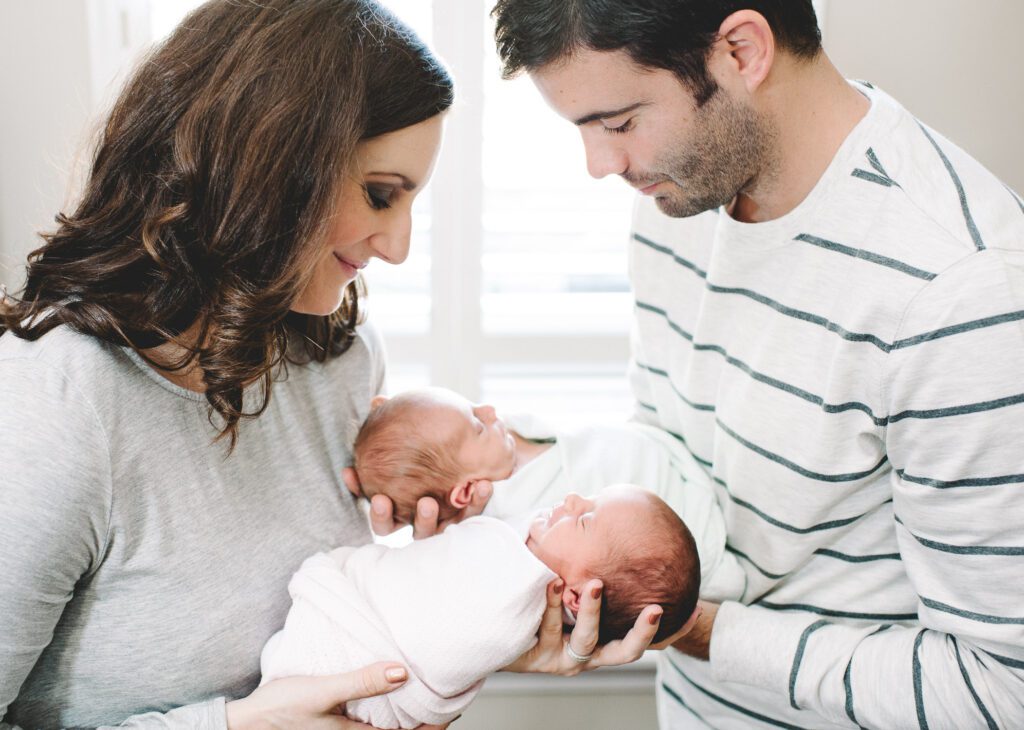 parents holding newborn twins in their home in Columbia, MO in front of window