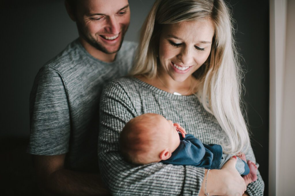 mom and dad looking down at newborn son in window at home in Columbia, MO