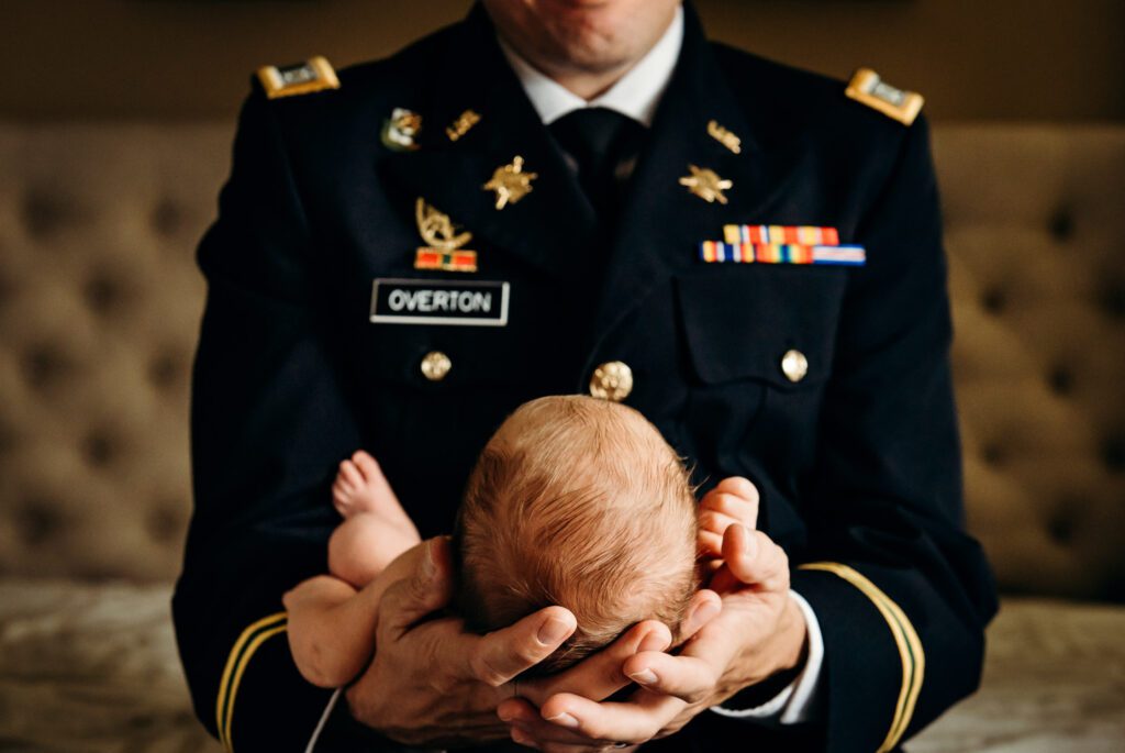 police officer in uniform holding newborn girl on bed