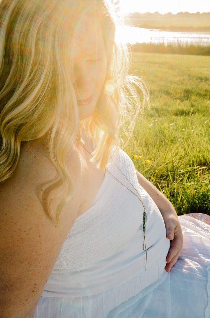 pregnant woman sitting in grassy field at sunset