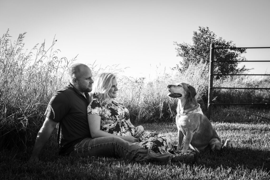 pregnant couple smiling at dog in field