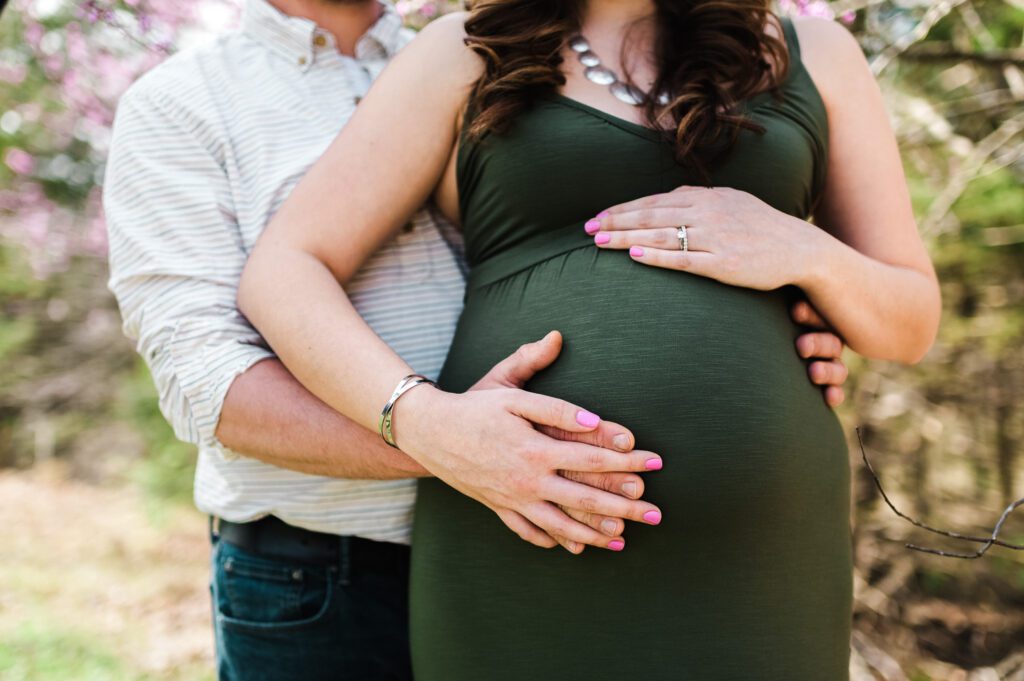 pregnant couple holding stomach in spring flowers