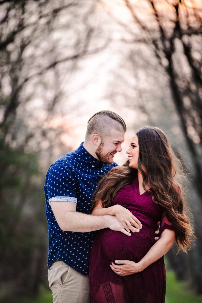 pregnant couple holding belly in wooded pathway