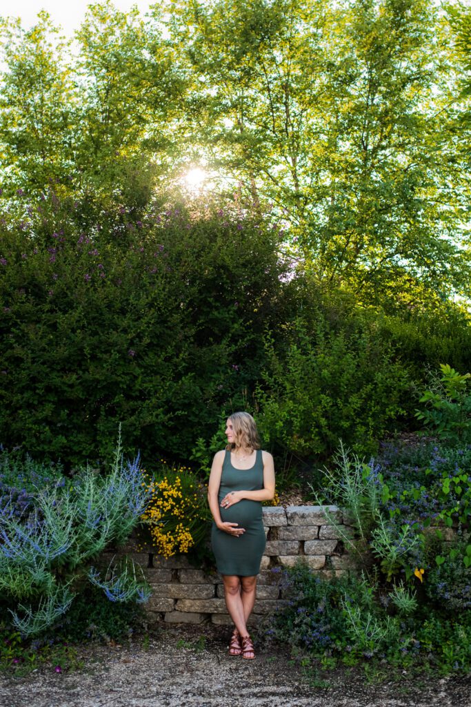 pregnant woman holding belly in front of flowers and rock wall
