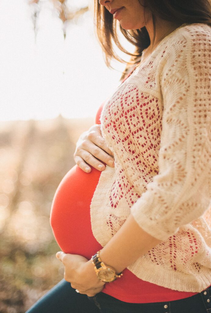 pregnant girl holding belly in field with cardigan