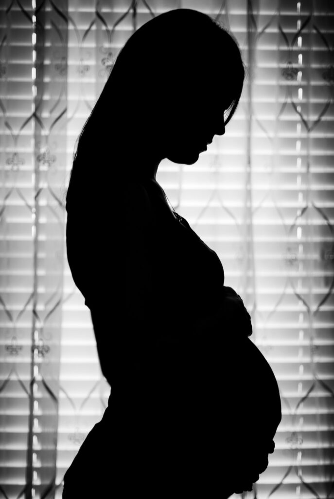 pregnant woman silhouette in front of window blinds