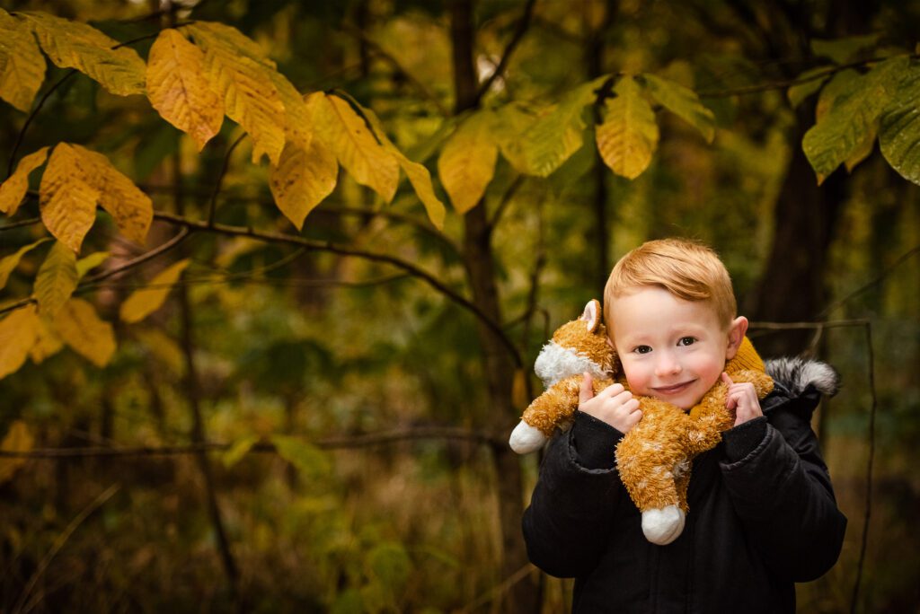 boy holding stuffed orange cat in woods