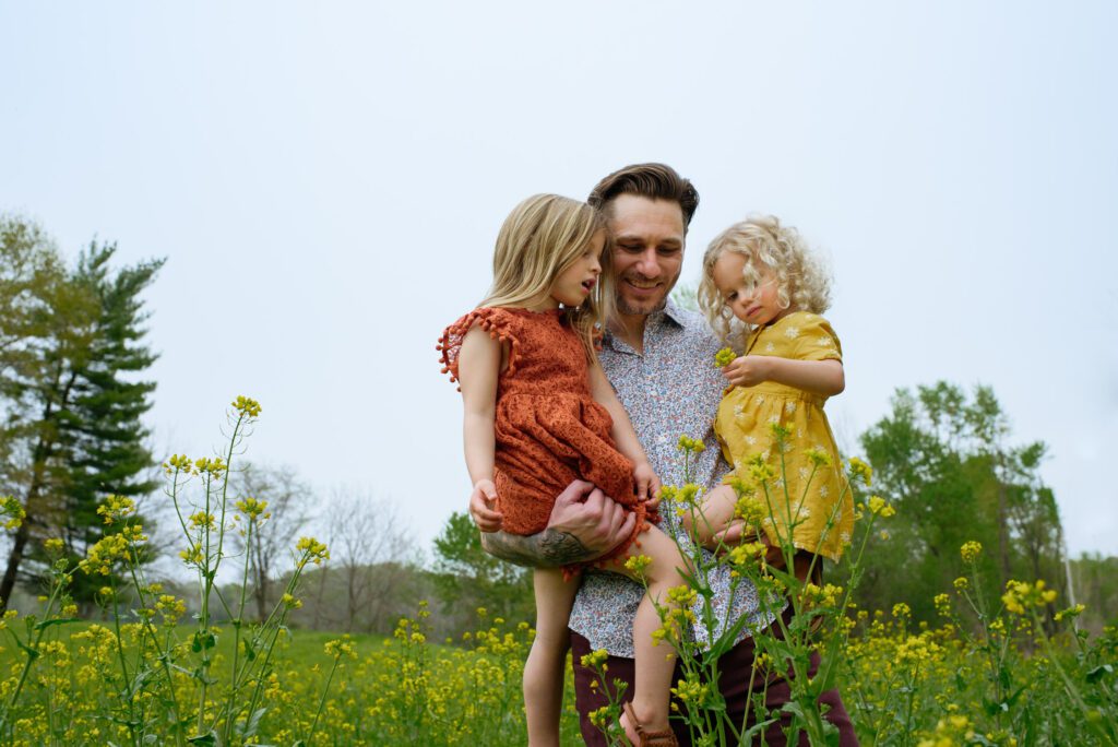 Dad holds two daughters in orange and yellow dresses.