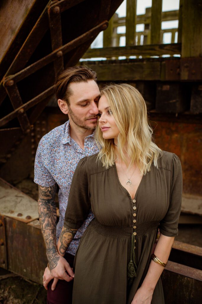Husband and wife snuggle on old bridge.
