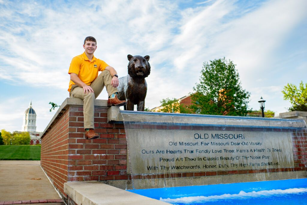 Senior guy sits by tiger statue and water fountain.