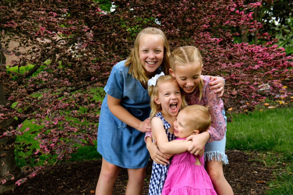 Four girls hug each other in front of a tri color beech tree
