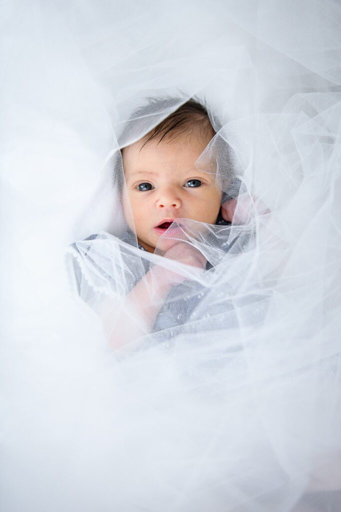 Newborn girl looks through tulle fabric