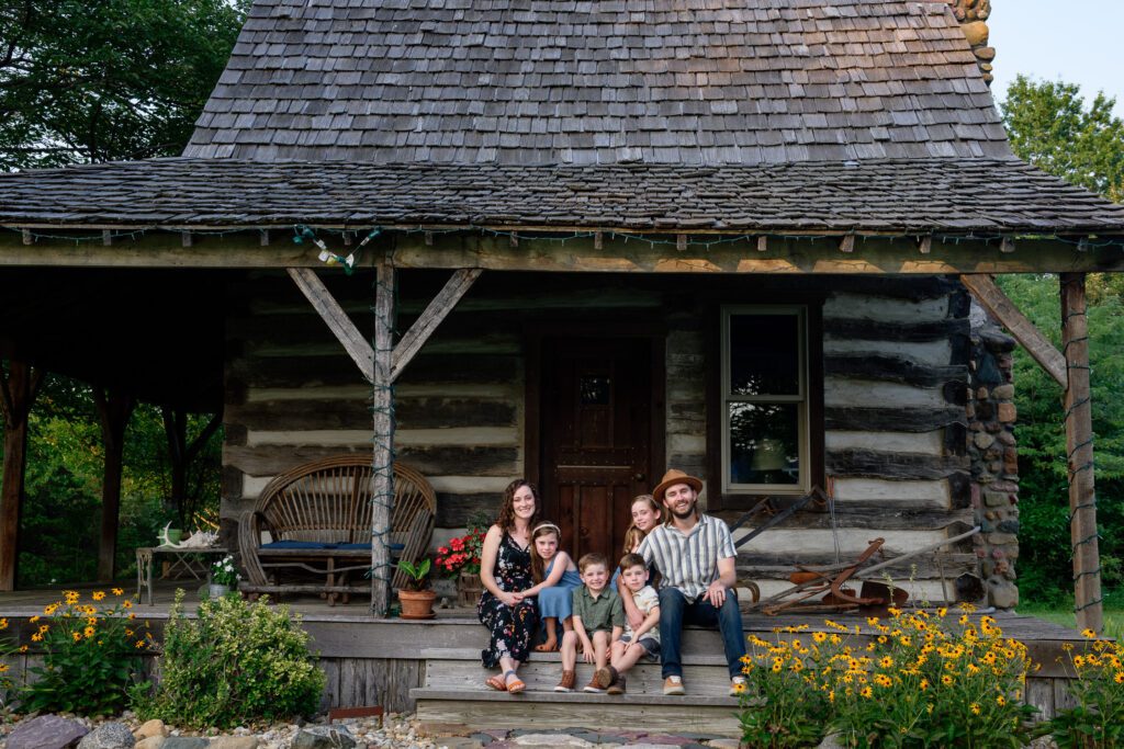 Family sit on the porch of an old log cabin