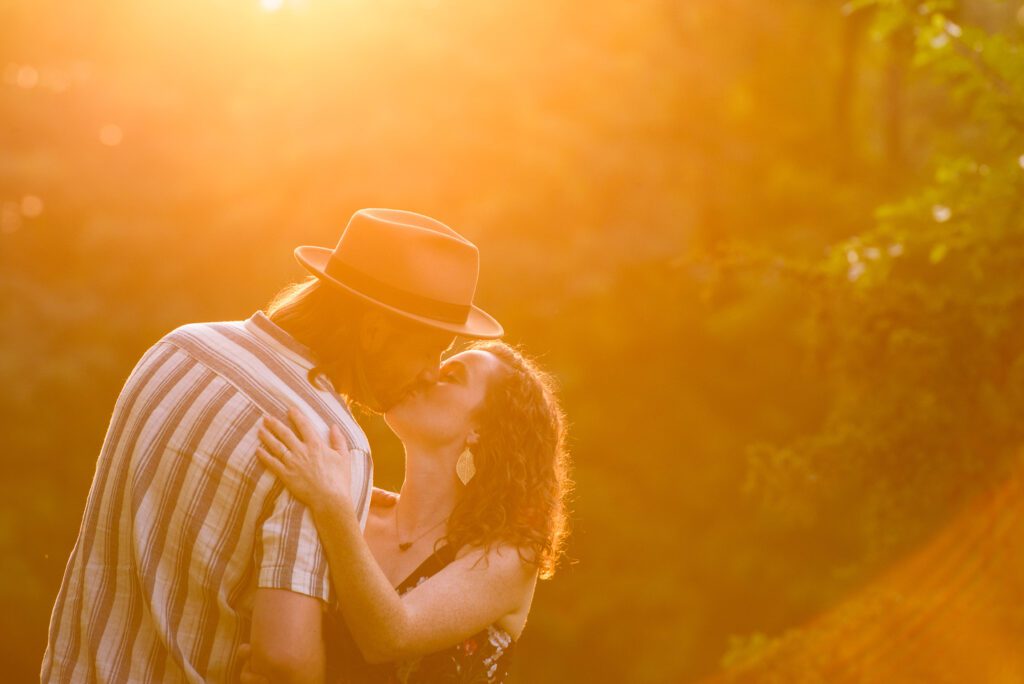 husband and wife kiss under the flare of the sun