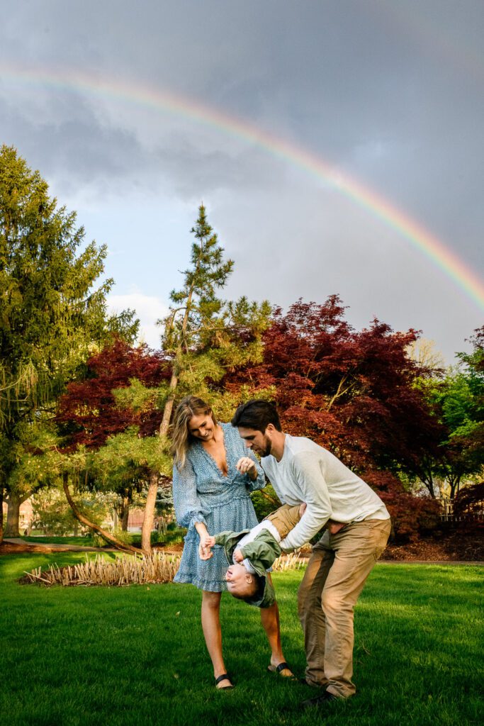 Family play with their young son with a rainbow in the sky.