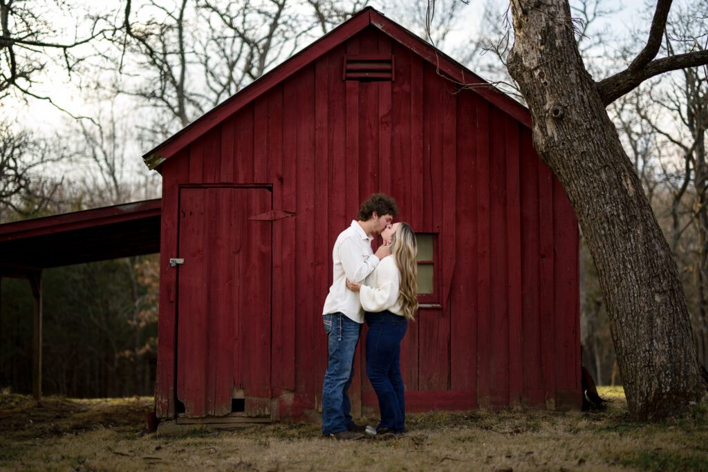 engaged couple kissing in front of red barn