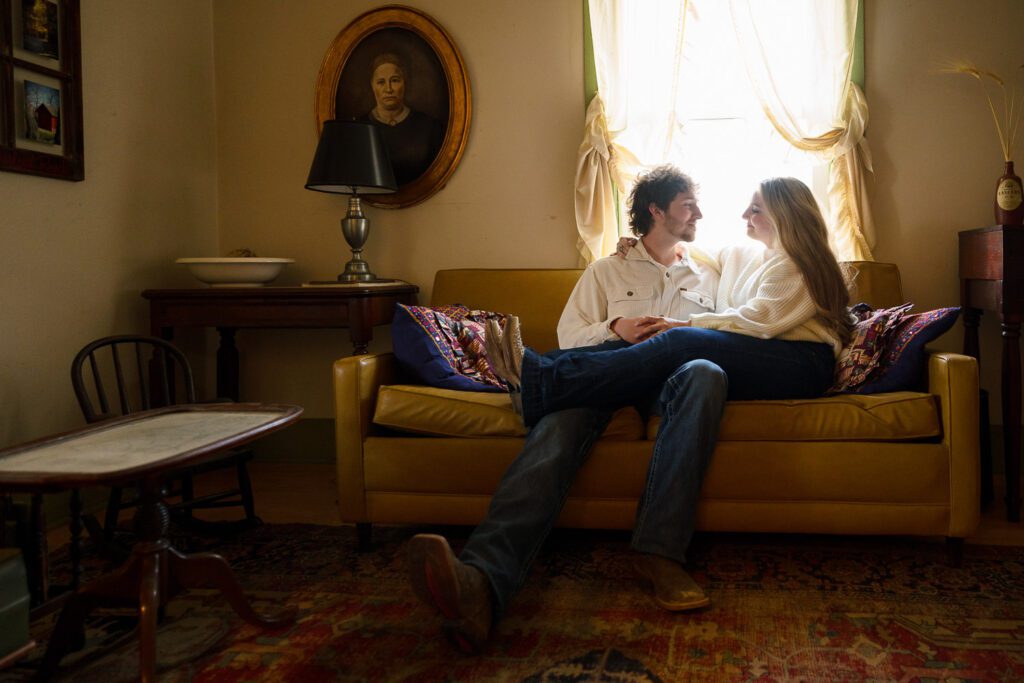 young woman sitting on fiance's lap in old farm house