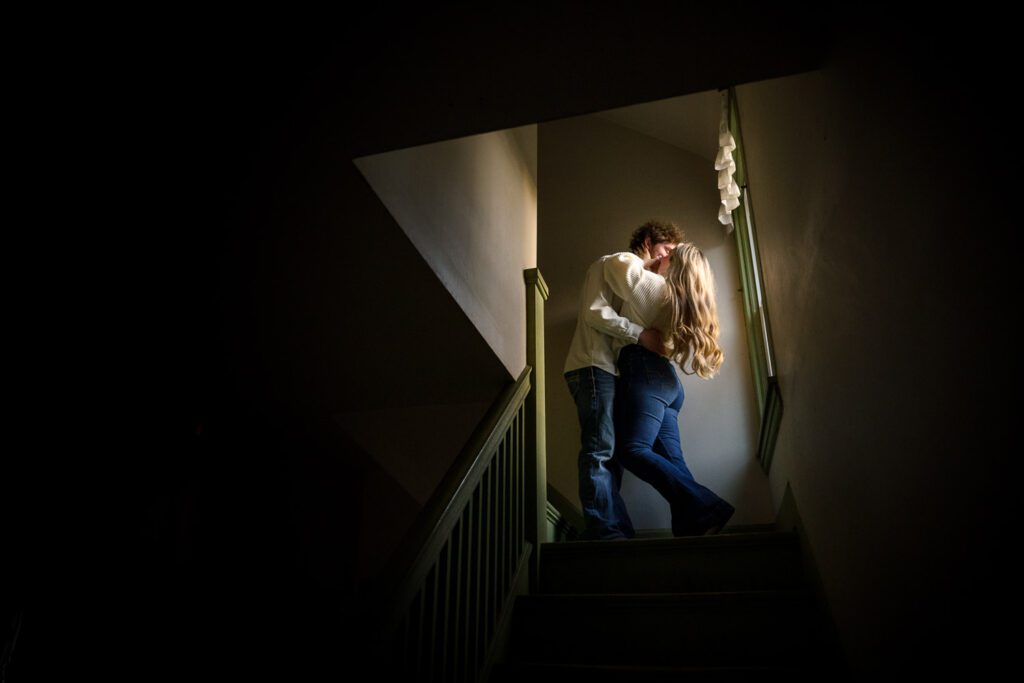 young couple kissing in stairwell with white sweaters and blue jeans