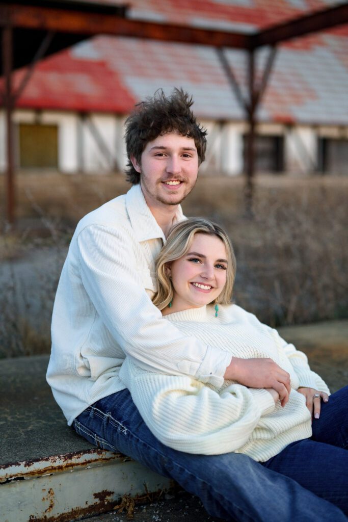 young couple sitting in front of old building with orange roof wearing white sweaters