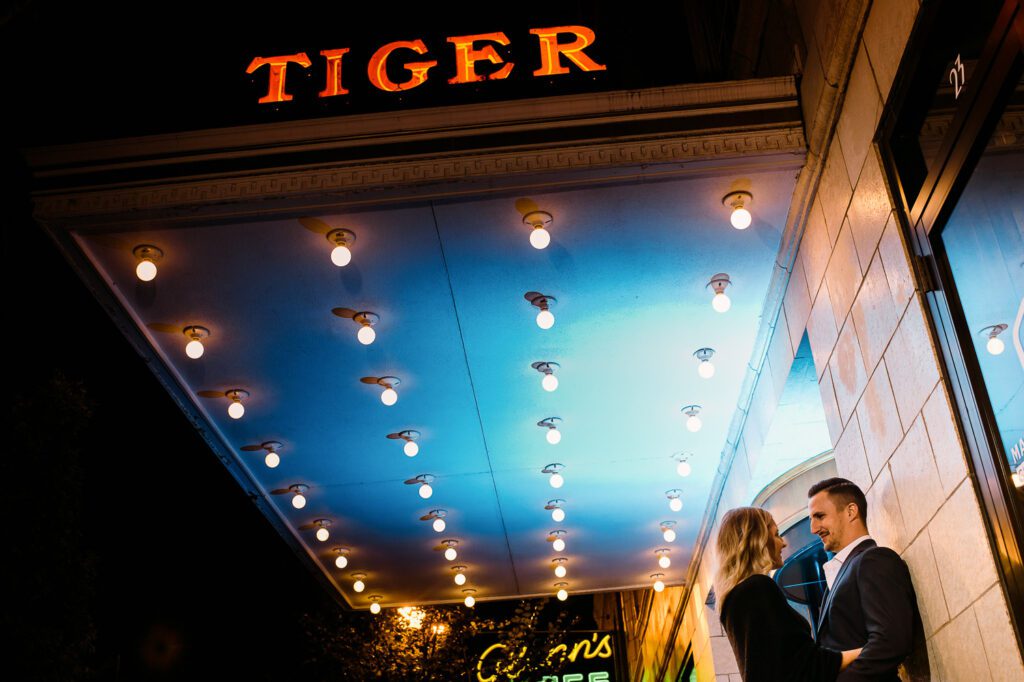 Couple in formal wear stand under Tiger Hotel Sign during Engagement