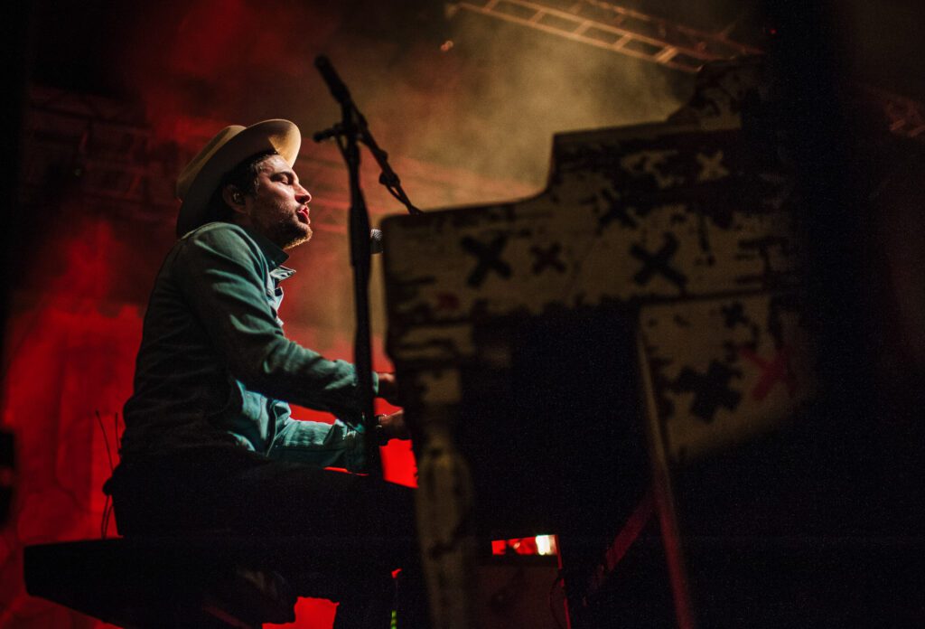 Scott Avett playing piano on stage at the roots and blues festival