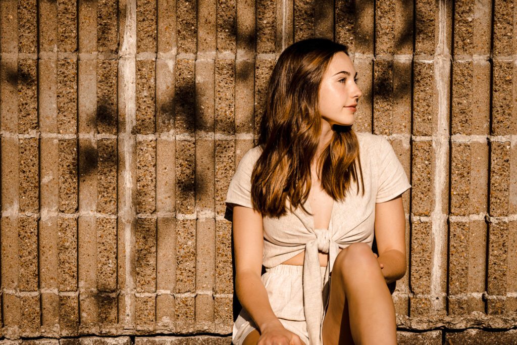 senior girl sitting against wall under beautiful sun