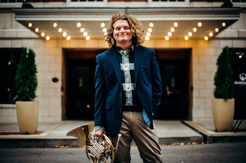 senior guy holding french horn in street