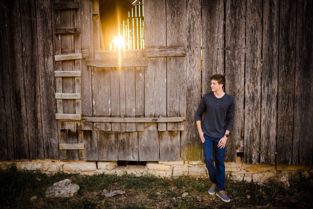 senior guy leaning on barn