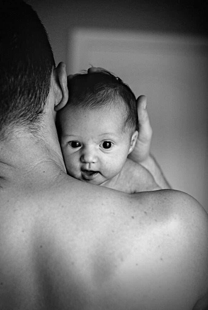 father with no shirt holding newborn baby smiling over his shoulder Columbia, MO