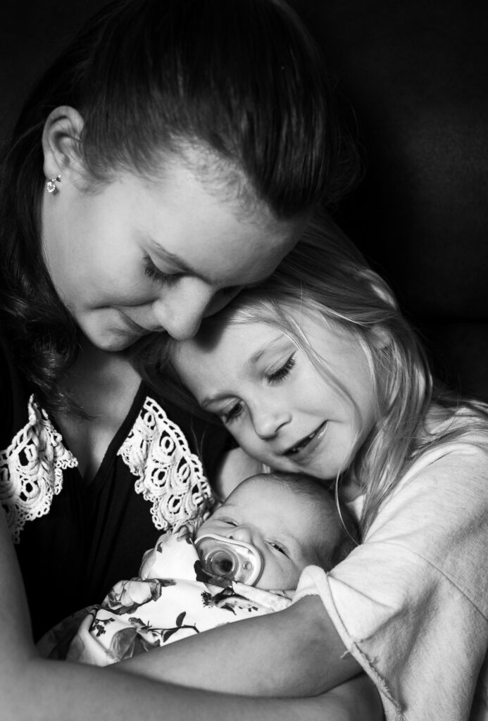 sisters snuggling newborn baby in Columbia, MO