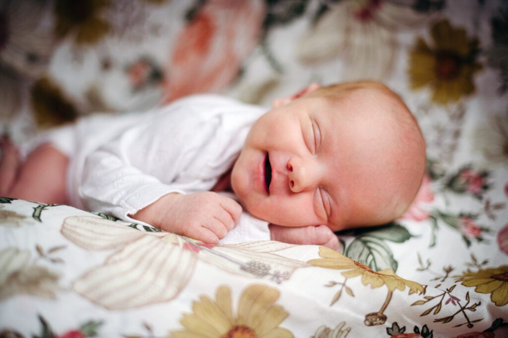 sleepy smiling newborn baby laying on colorful floral blanket