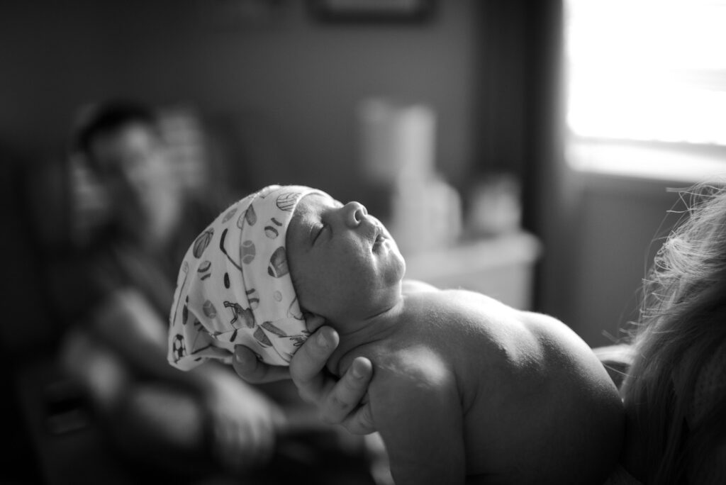 newborn baby wearing tiny hat with sports theme in window silhouette
