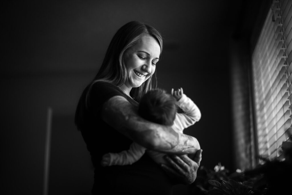 mother with tattoos smiling at newborn baby in window