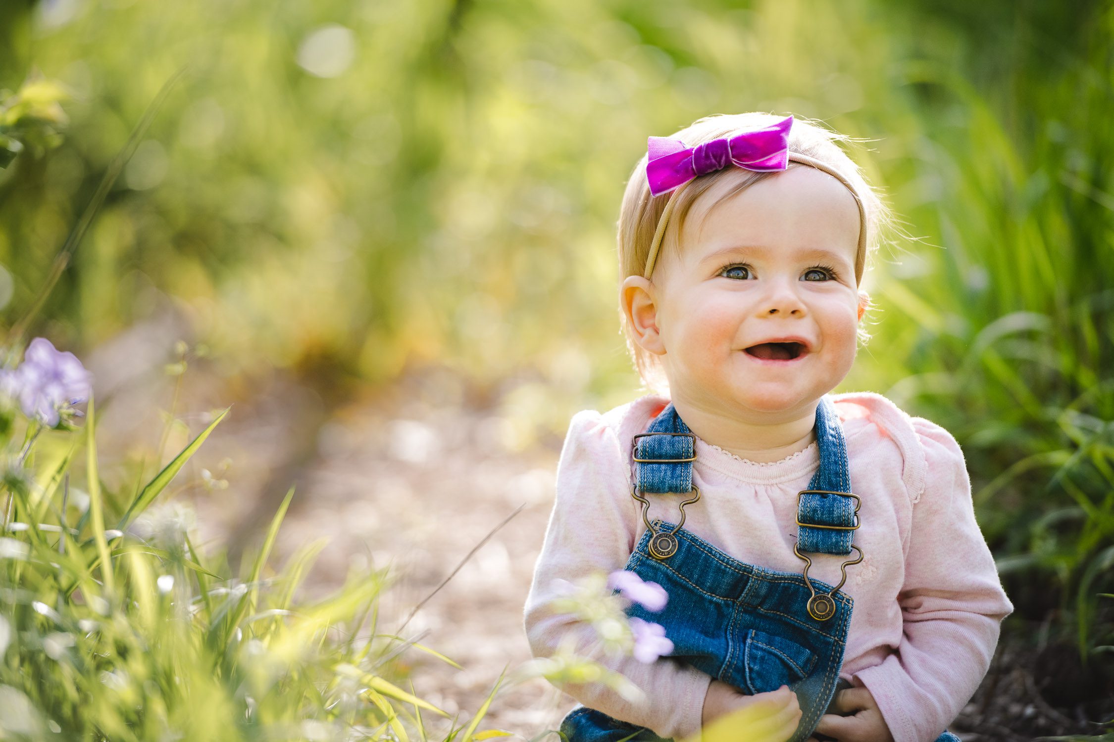 Daughter with bow in her hair sitting down in the grass for family photographs - Kasmann Family Photos by Schaefer Photography in Capen Park, Columbia, Missouri.