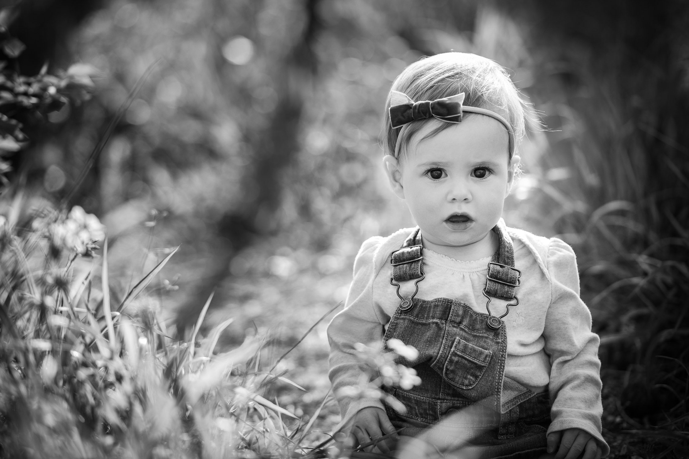 Daughter with bow in her hair sitting down in the grass for family photographs -Black and white photo- Kasmann Family Photos by Schaefer Photography in Capen Park, Columbia, Missouri.