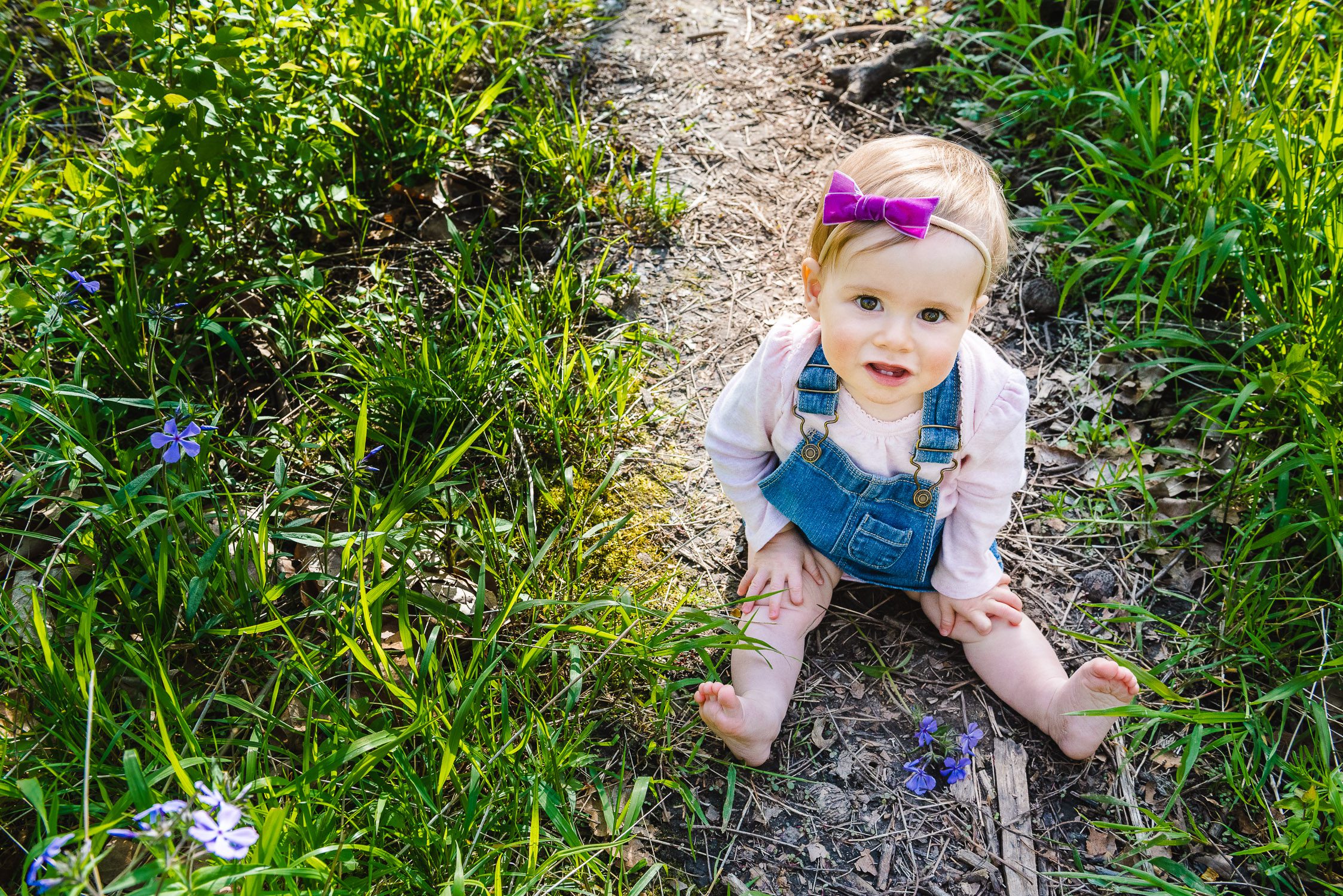 Daughter with bow in her hair sitting down on a trail at Capen Park for family photographs - Kasmann Family Photos by Schaefer Photography in Columbia, Missouri.