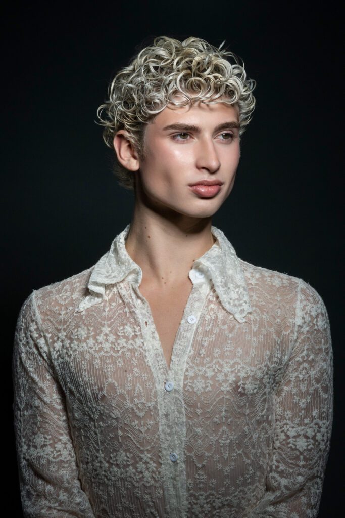 Male model zachary wilmore poses wearing white sheer top on black