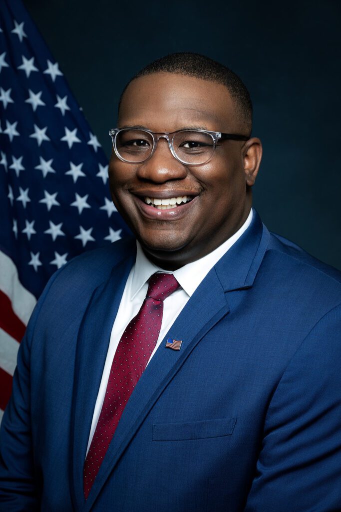 Black male wearing navy suit red tie with american flag