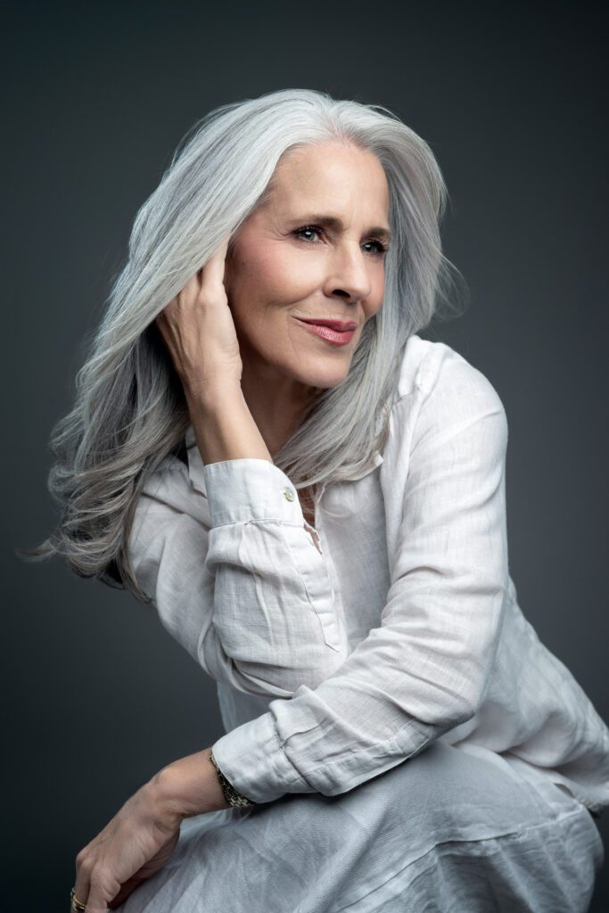 woman with gray hair wearing white shirt with hand next to face