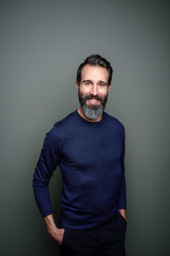 guy with dark hair and beard wearing blue sweater headshots