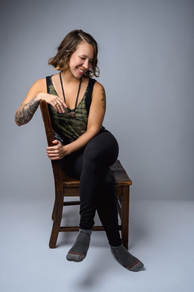 Woman with tattoos and brown hair with green tank top poses for headshot
